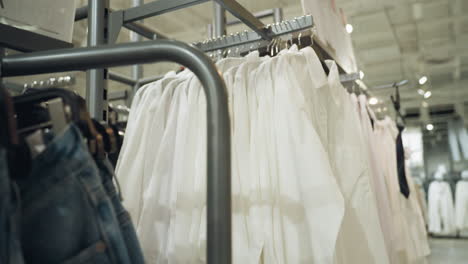 a clothing store showcasing a variety of clothes on racks, including neatly hung white shirts, jackets, and jeans. captured with a handheld camera, the video highlights the organized layout