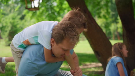 Verspielter-Sohn,-Der-Auf-Dem-Rücken-Reitet,-Blonder-Mann-In-Nahaufnahme.-Lächelnder-Vater-Hebt-Süßen-Jungen-Hoch.