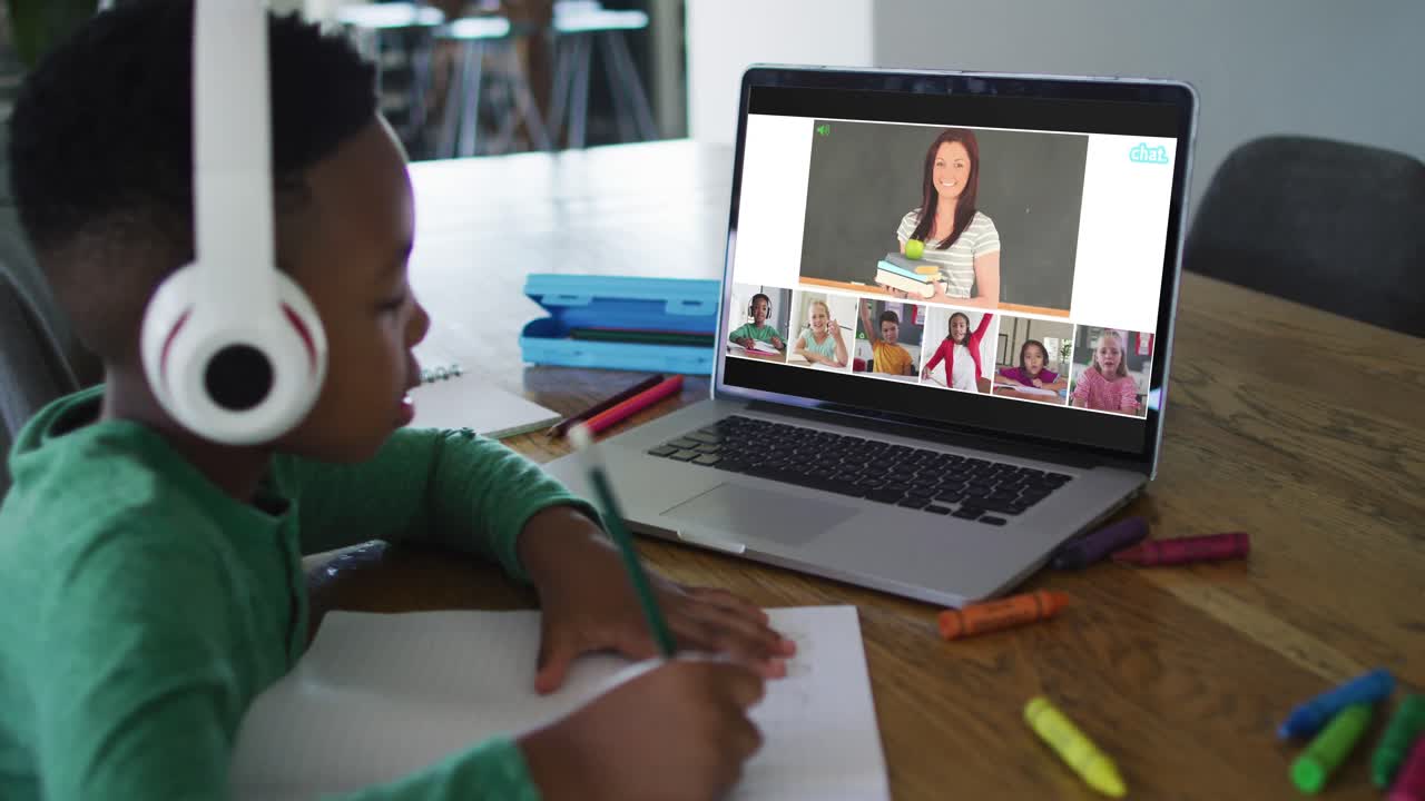 Schoolboy using laptop for online lesson at home, with diverse teacher and class on screen