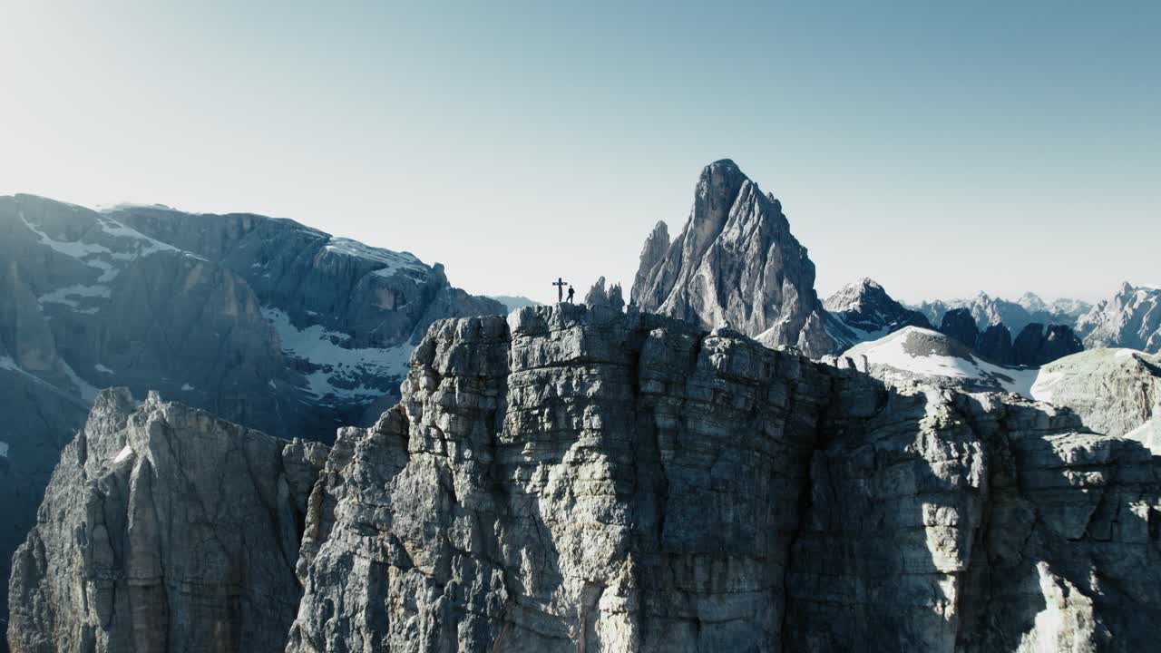 Riprese aeree di un alpinista in piedi su una vetta mentre la telecamera si allontana per rivelare la catena montuosa.