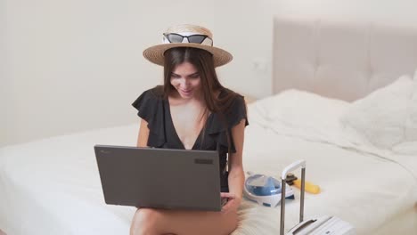 beautiful-girl-in-swimsuit-and-hat-with-a-suitcase-chooses-on-a-laptop-where-to-go-on-vacation