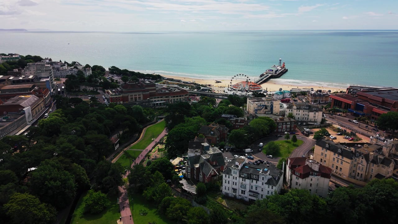 Drohnenaufnahmen der Küste von Bournemouth, die Seebrücke, Sandstrand, türkisfarbenes Meer, Gebäude im Stadtzentrum, Straßen, Hotels und grüne öffentliche Gärten zeigen. Nützlich für Themen wie Großbritannien-Reisen, Tourismus
