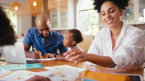 Familia-Alrededor-De-Una-Mesa-En-Casa-Usando-Una-Computadora-Portátil-Con-Padres-Ayudando-A-Los-Niños-Con-La-Tarea-De-Ciencias