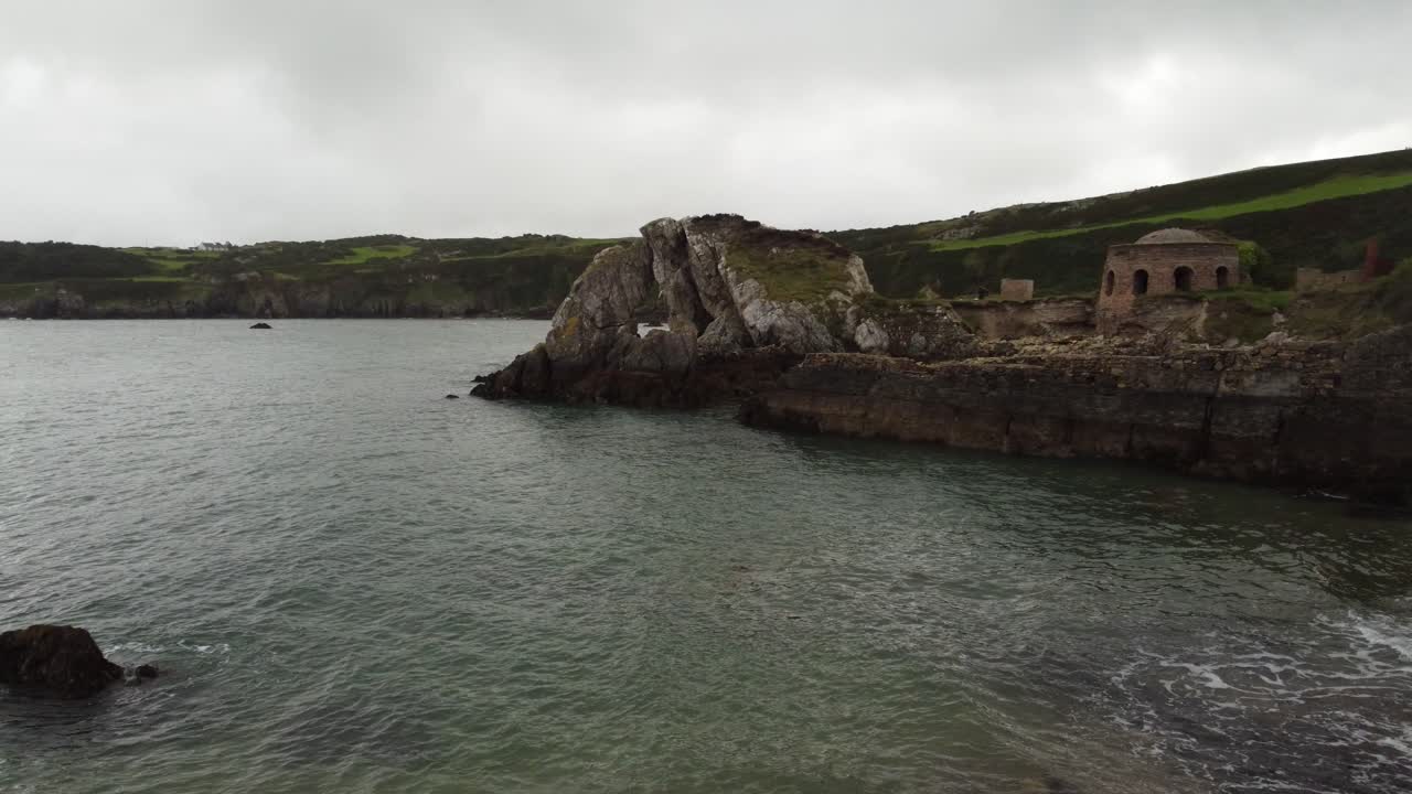 Vista aerea inversa che vola a bassa quota verso la baia di Traeth Porth Wen Beach, un ex sito di mattoni abbandonato sulla costa del Mare d'Irlanda.