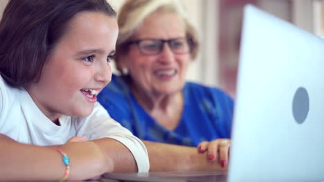 Niña-Positiva-Enseñando-A-La-Abuela-Viendo-Videos-En-Una-Computadora-Portátil-En-Casa