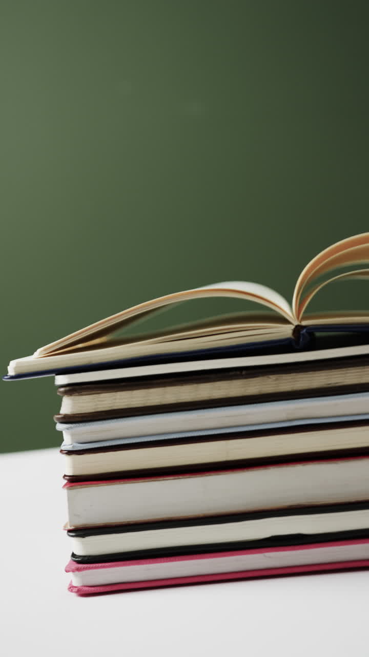 Vertical video of stack of books and notebooks with copy space on green background