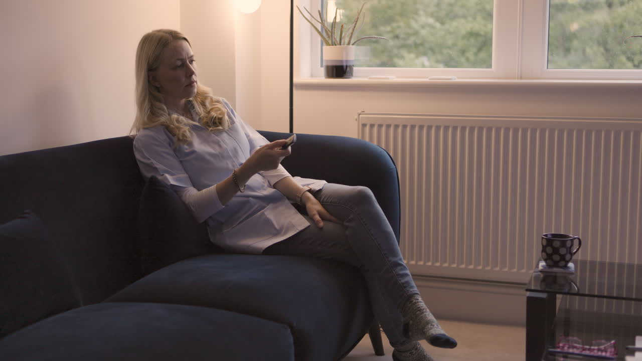 Kvinde slapper af på sofaen med fjernbetjening