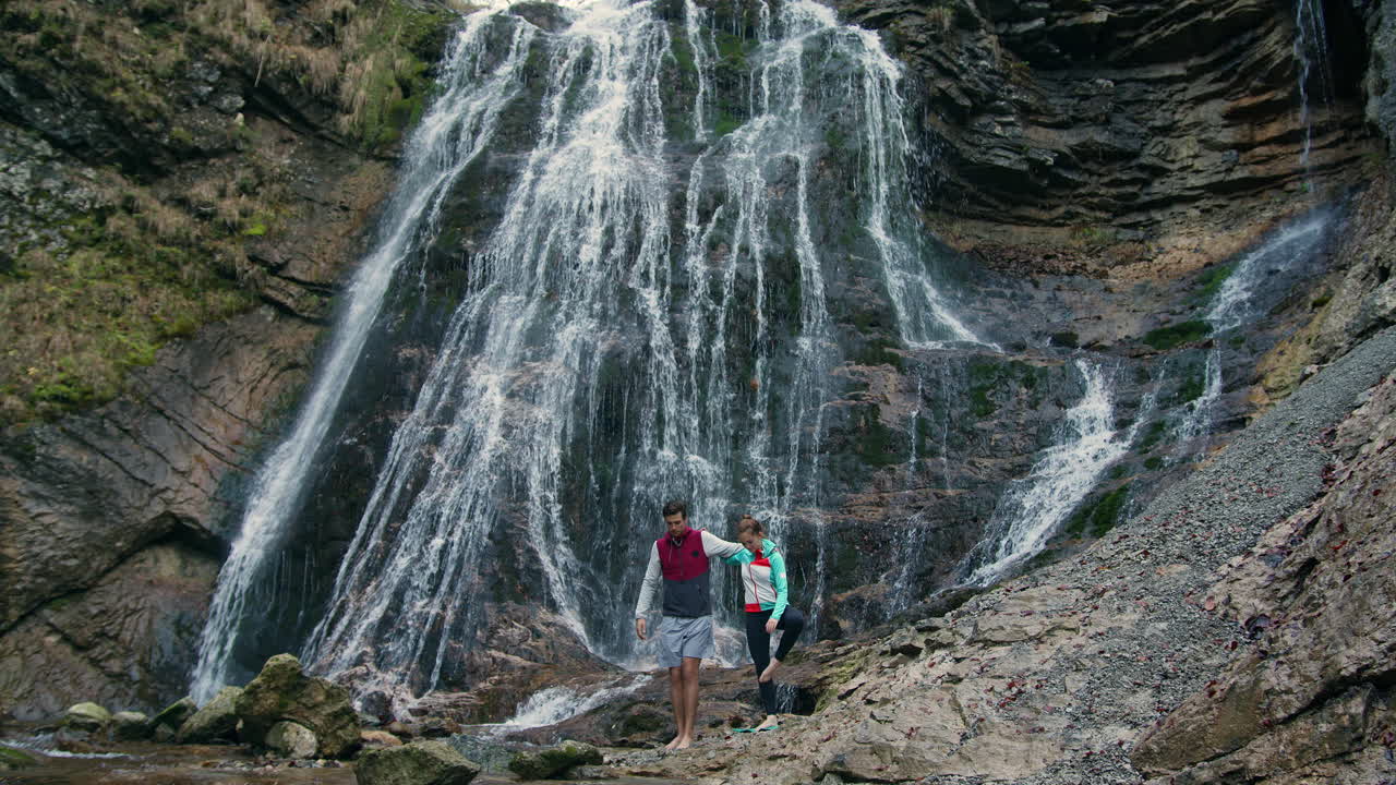pareja en una postura de yoga de árbol, ejercicios de equilibrio matutino junto a una cascada, toma amplia
