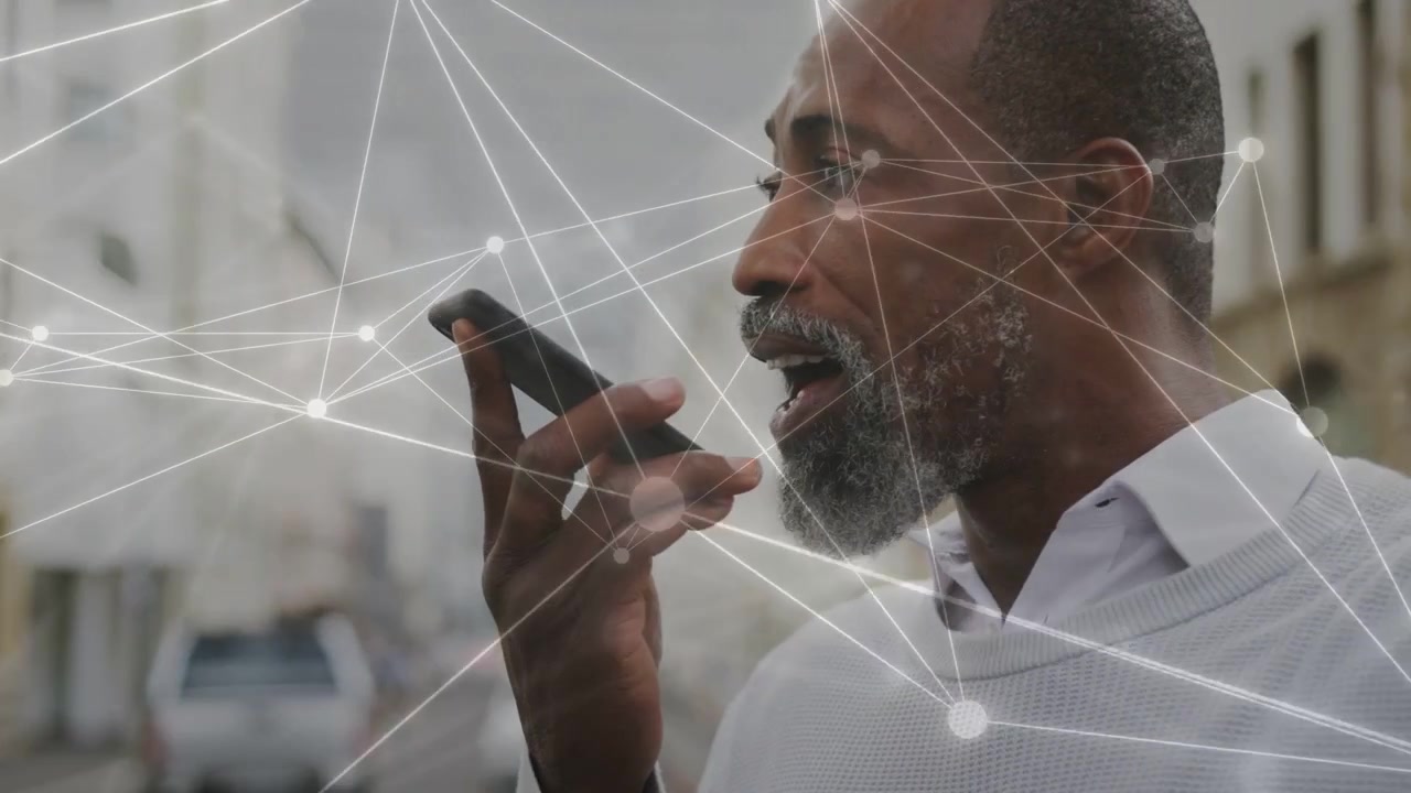 Un homme d'âge mûr porte son téléphone à sa bouche, parlant et activant un réseau de nœuds animé affichant des connexions technologiques.