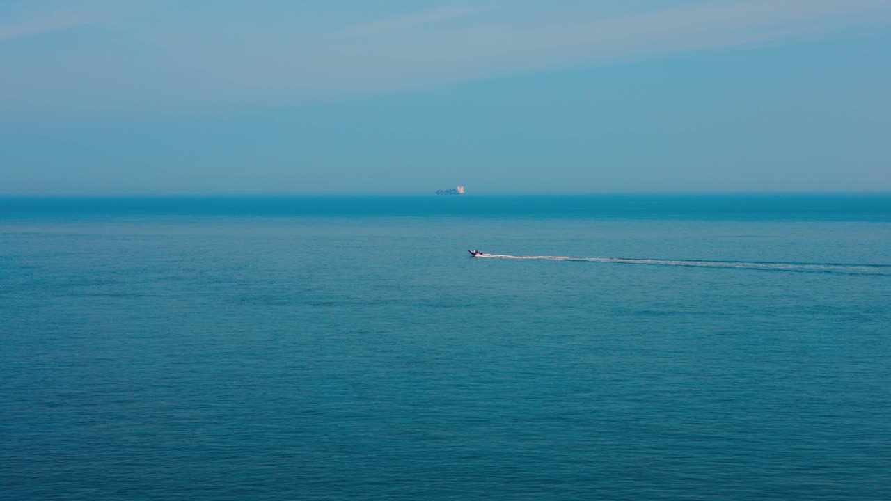 穏やかな青い海を遠くのボートが航行する、リラックスできる海岸の風景。