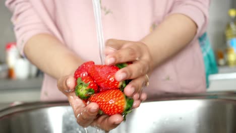 Women-hand-cleaning-strawberry-with-fresh-water-,