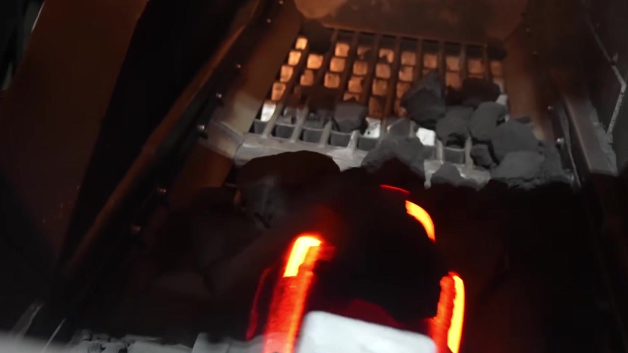 Glowing red-hot castings visible inside sand molds on shakeout conveyor at foundry