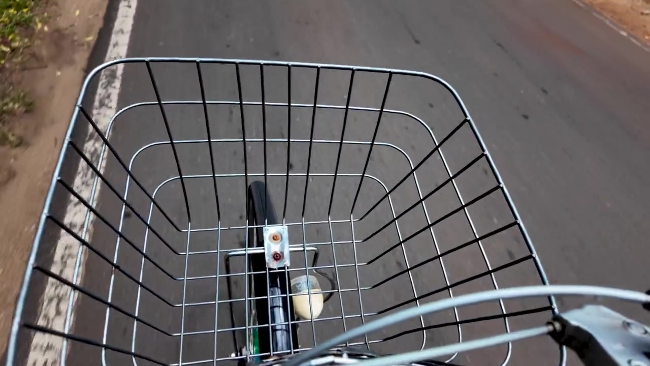 Ripresa in soggettiva che cattura un cestino da bicicletta e una strada aperta, evocando un senso di libertà e avventura su due ruote.