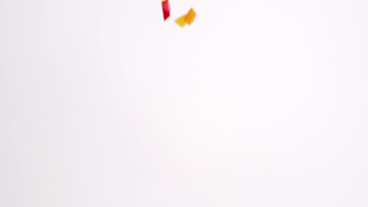 밝은 색상의 빨간색, 녹색, 노란색 및 주황색 깍둑썰기한 피망 신선한 야채 조각이 흰색 배경에 슬로우 모션으로 비가 내리고 있습니다.