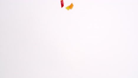 brightly colored red, green, yellow and orange diced bell pepper fresh vegetable pieces raining down on white backdrop in slow motion