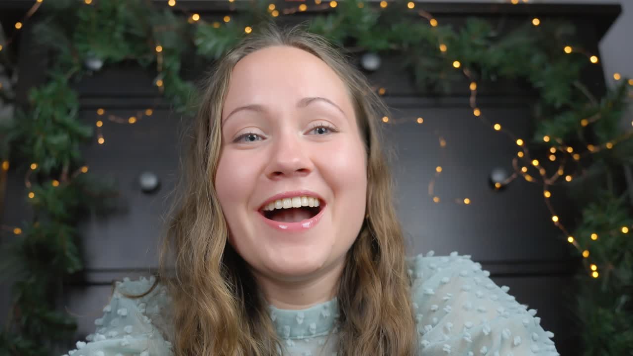 Close-Up of Young Woman's Happy Surprise Opening a Present with Festive Decorations in the Background