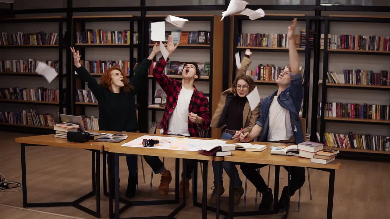 Slow motion of students throwing the sheets of paper up after hours of studying in uni library. Happy and free students who don't want to study or are celebrating the start of vacations. Congratulating each other with finishing studying