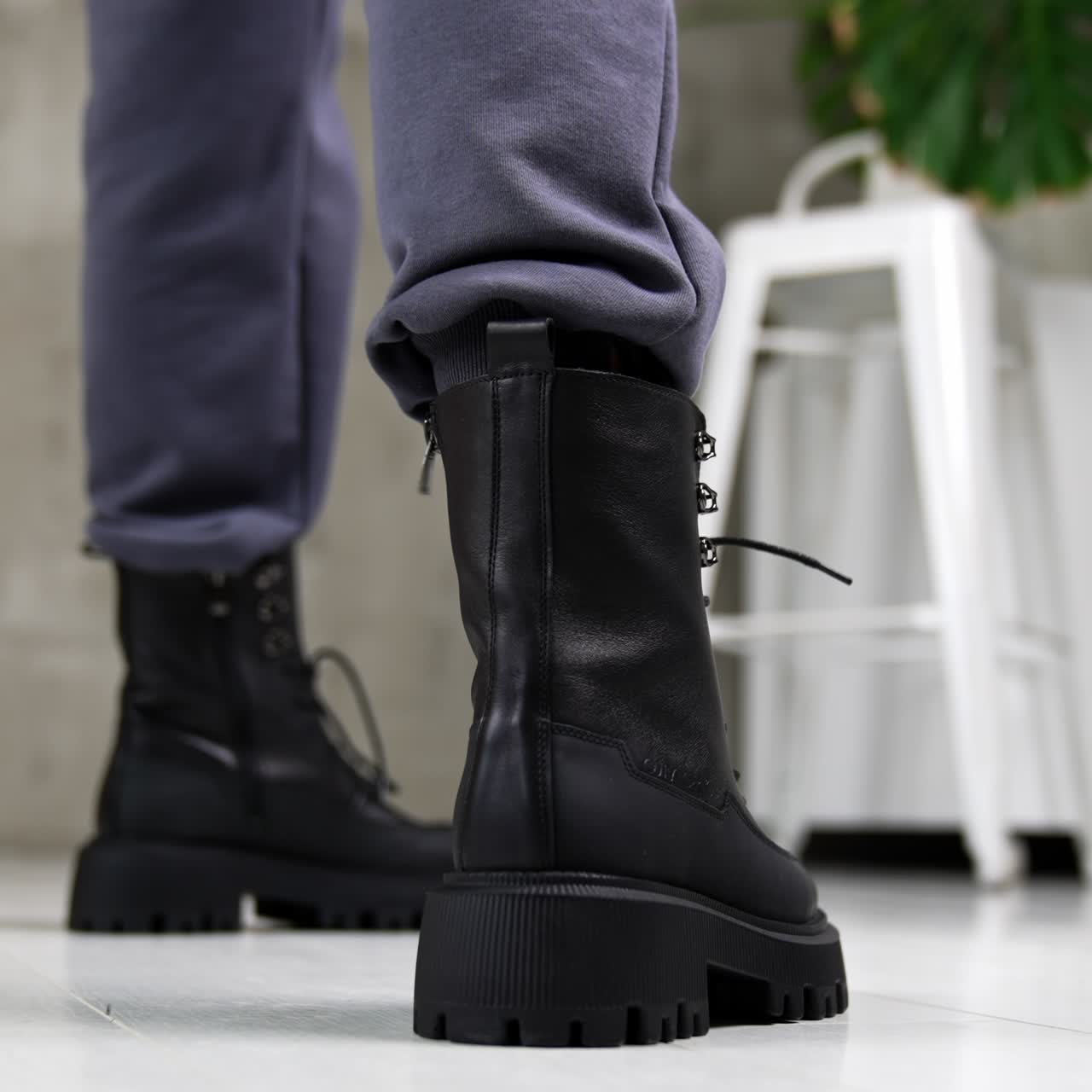 Black laced army boots demonstration. Close up. Model wearing grey pants and leather massive footwear in studio