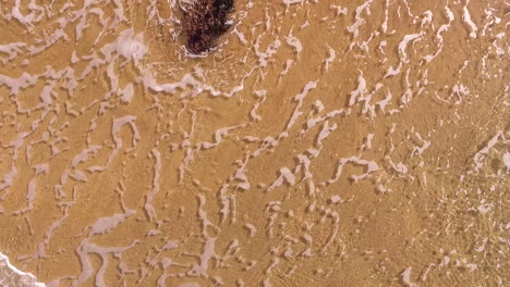 aerial shot looking down onto waves on a sandy beach as the camera lifts up slowly