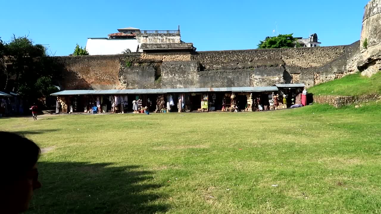 mujer turista caminando por el prado de la antigua fortaleza de ngome kongwe con algunas tiendas locales detrás