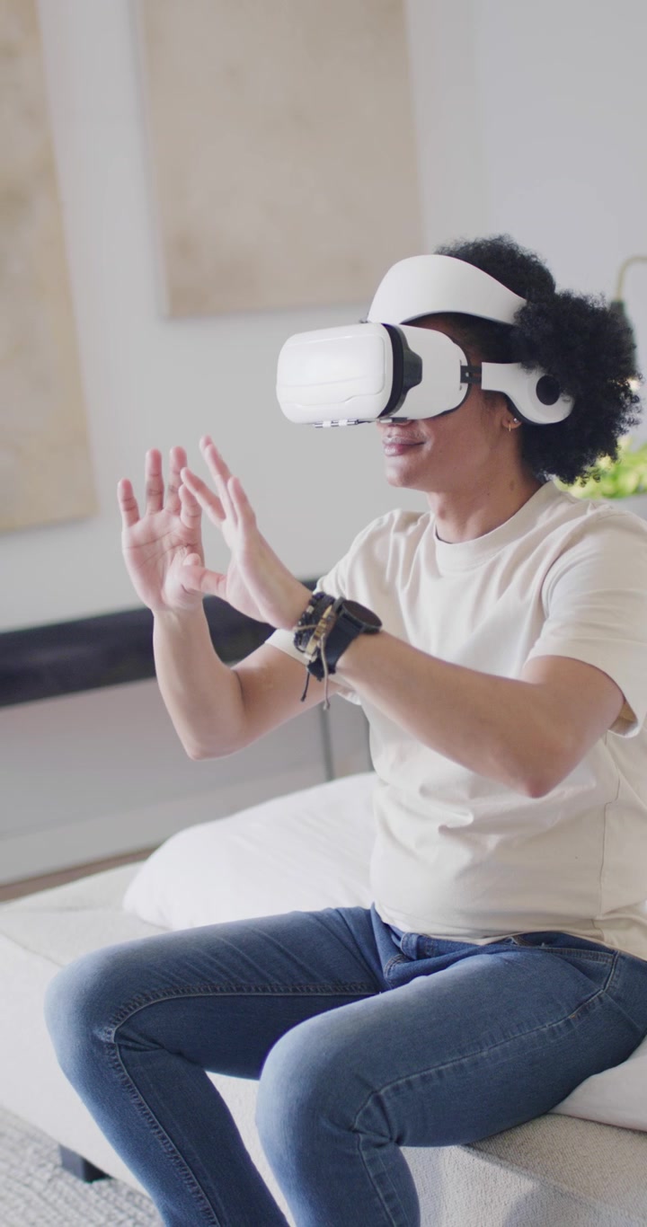 Video verticale: Uomo afroamericano che indossa un visore VR bianco e usa controlli virtuali a casa