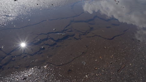 Flowing-rainwater-on-broken-asphalt-road-on-sunny-day,-close-up