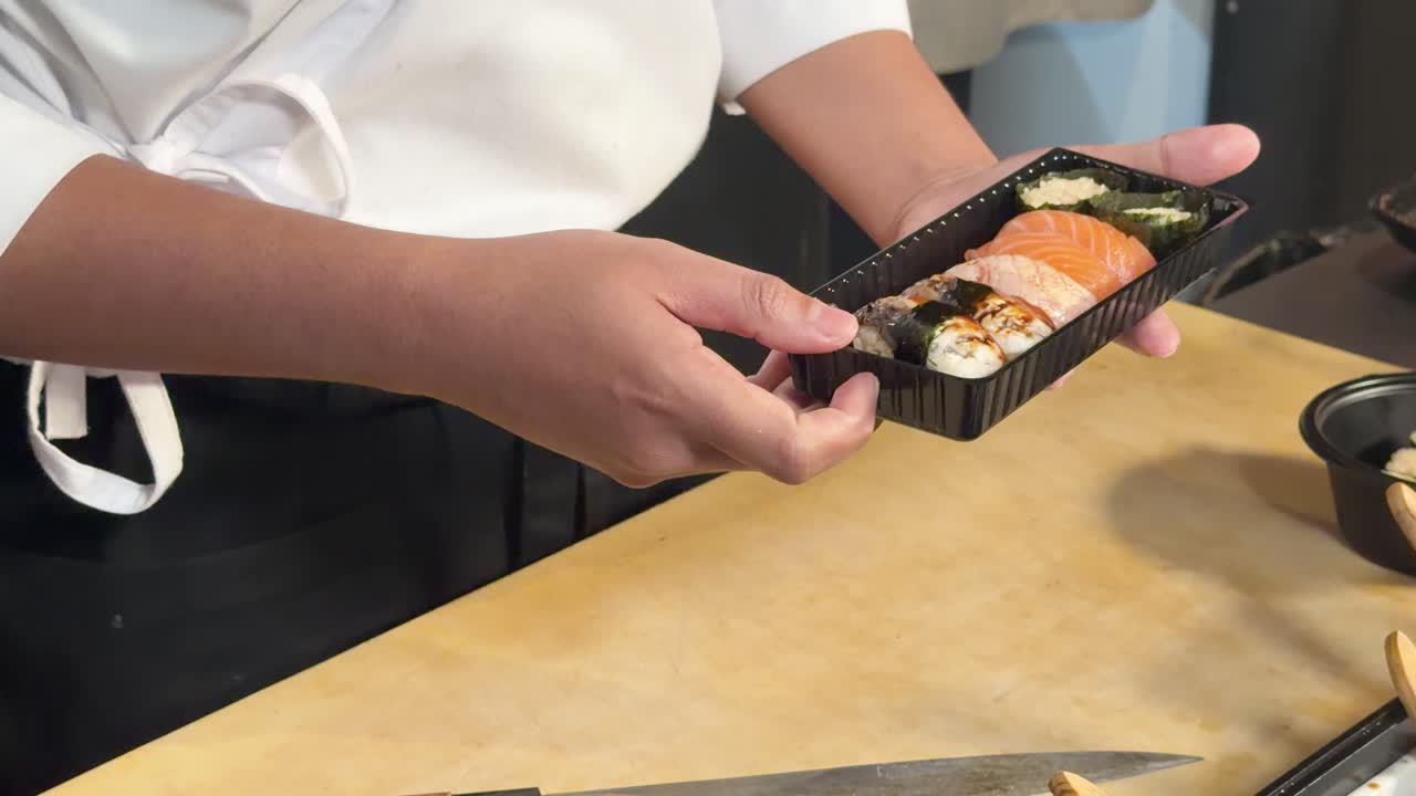 Primo piano di uno chef di sushi che spennella la salsa su un assortimento di nigiri bento sotto una luce soffusa da studio