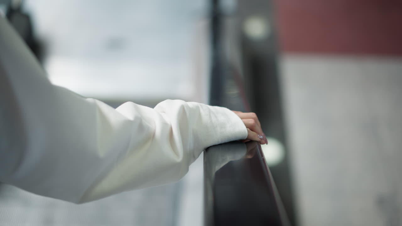반이는 레일링에 부드럽게 어있는 손의 클로즈업, 현대 실내 공간의 흐릿한 배경과 함께 은 손과 수갑 세부 사항을 포착합니다.