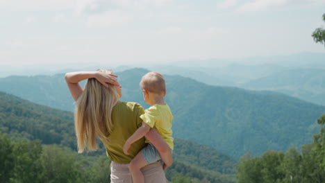 woman holds little son and adjusts hair at mountain resort