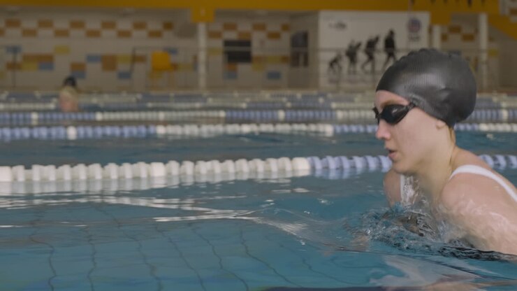 Primo piano laterale di una giovane donna che nuota attivamente a rana in piscina coperta.