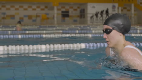 Nahaufnahme-Einer-Seitlichen-Kamerafahrt-Einer-Jungen-Frau,-Die-Brustschwimmen-Aktiv-Im-Hallenbad-Schwimmt