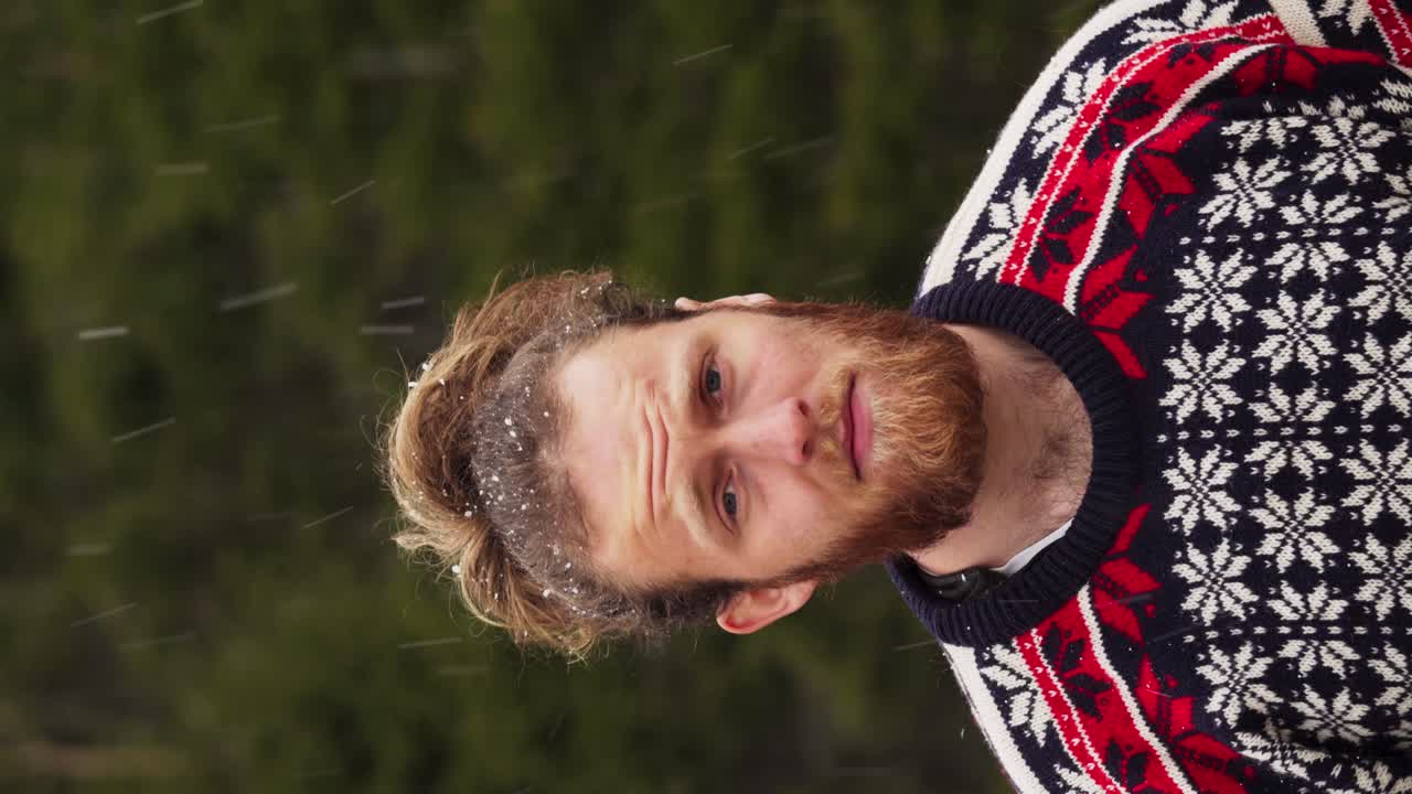 - 수직 수염과 긴 머리카락의 유럽 남자가 눈이 내리면서 야외에 서 있습니다.