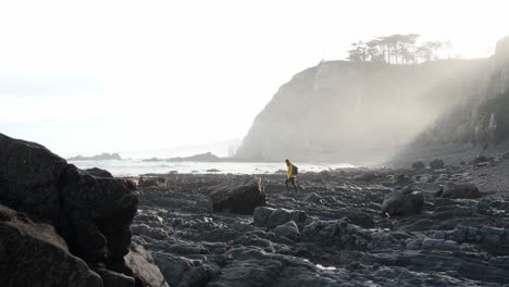 Female-traveler-walking-on-rocky-seashore-surrounded-by-sharp-cliffs