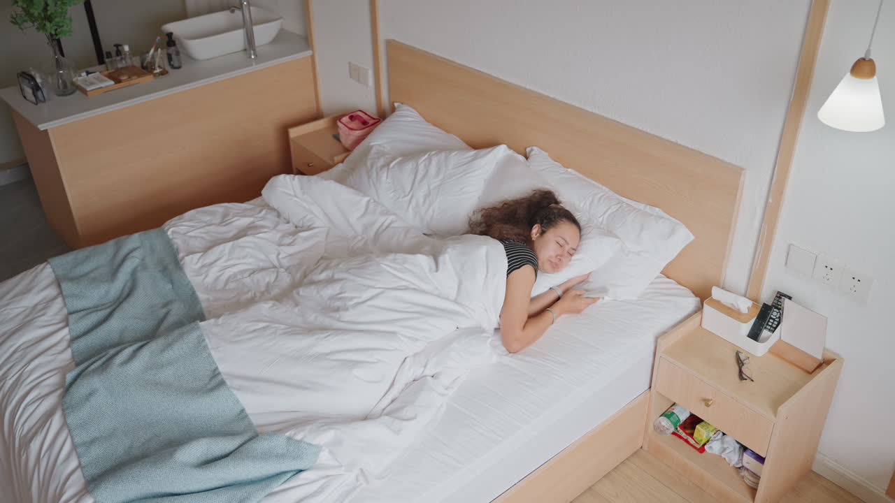 햇살 가득한 호텔 객실에서 스마트폰을 스크롤하는 여성, 새하얀 침구와 이불 속에서 부드럽게 깨어남, 침대 옆 램프와 충전 케이블, 여행 일정과 모닝 커피를 계획 중, 부드러운 나무 톤과 미니멀한 디자인, 차분한 혼자만의 시간