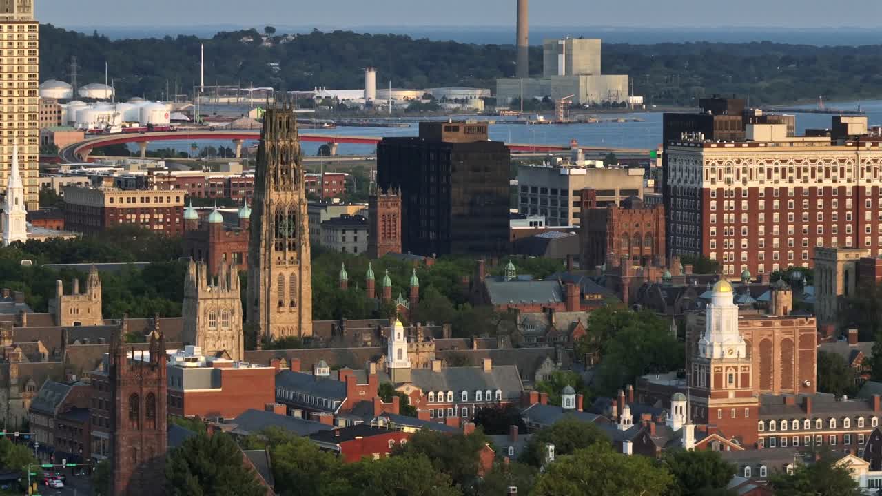 Downtown New Haven, Connecticut, showing historic university buildings, modern office towers and industrial waterfront along Long Island Sound. Sunset time. Aerial rising wide shot