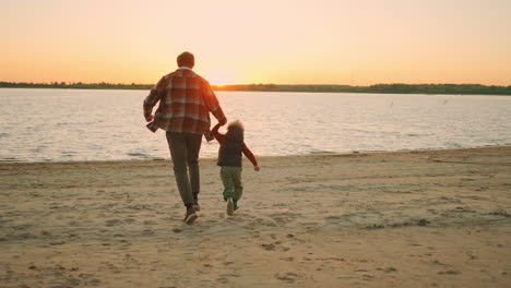 happy-little-boy-and-his-father-are-running-over-river-shore-in-sunset-happiness-of-family-weekend