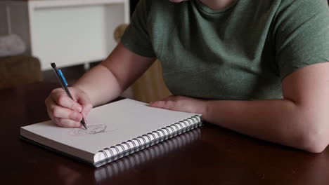 Una-Mujer-Caucásica-Esboza-Un-Rostro-Femenino-En-Un-Cuaderno-De-Bocetos