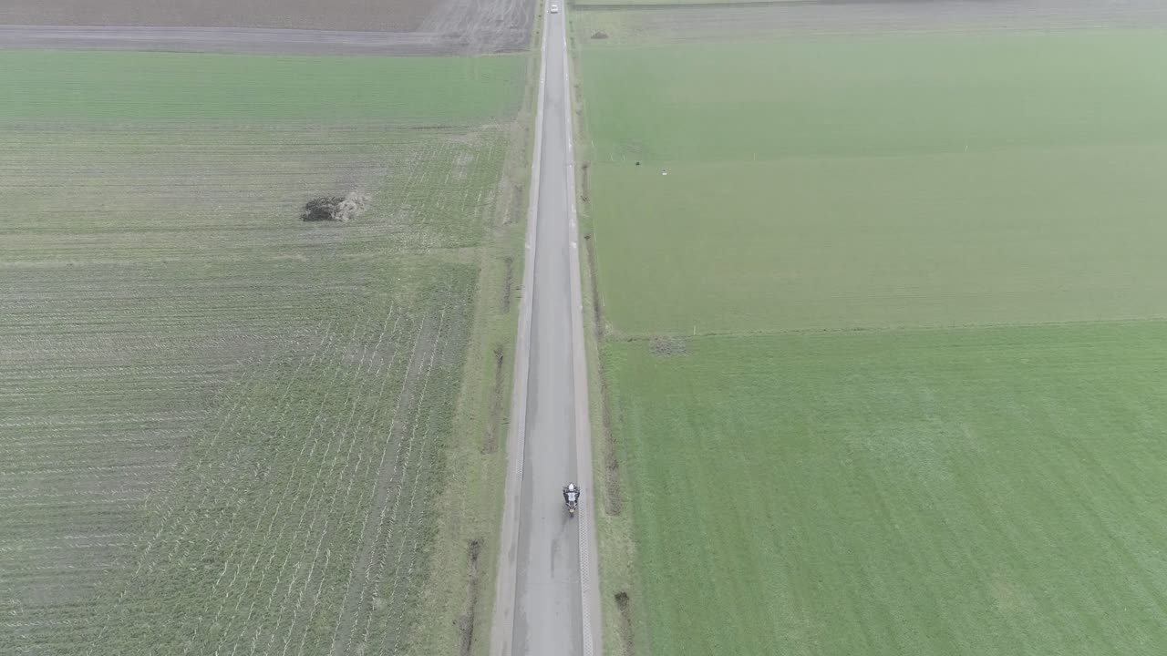 From above drone shot of motorcyclist driving down a farm road