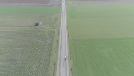 from above drone shot of motorcyclist driving down a farm road