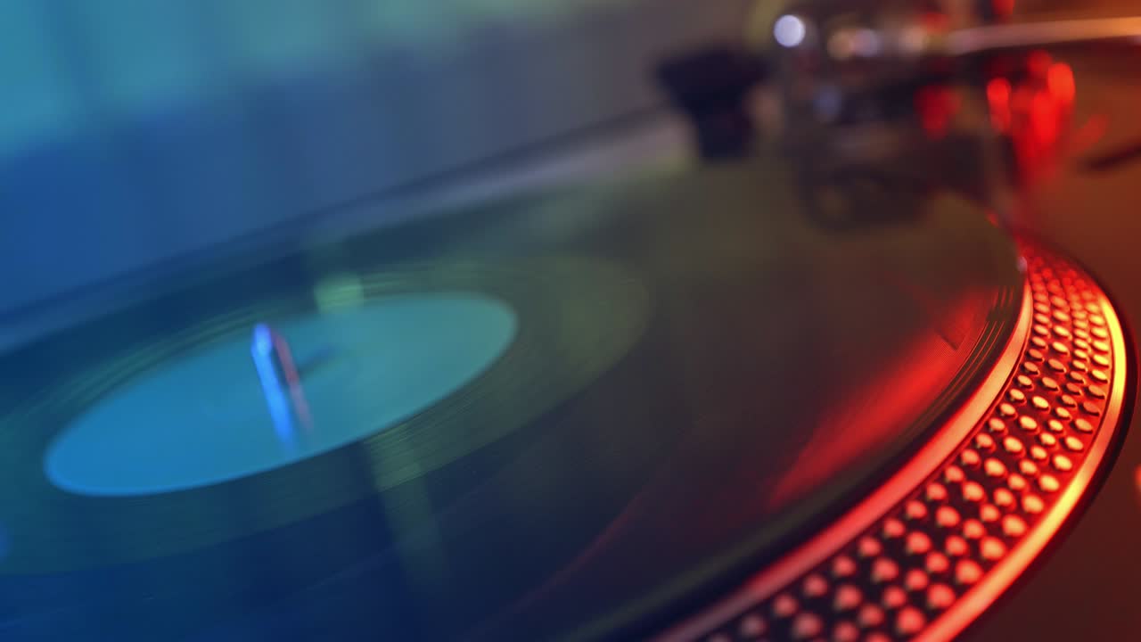 비닐 플레이어 턴테이블: 회전하는 비닐 레코드의 조각, 바늘을 클로즈업으로 가진 스타일러스, 바늘과 비닐 판을 멈추는, 매크로, 전면 뷰, 빨간색과 파란색 빛의 배경에서 흐릿한.