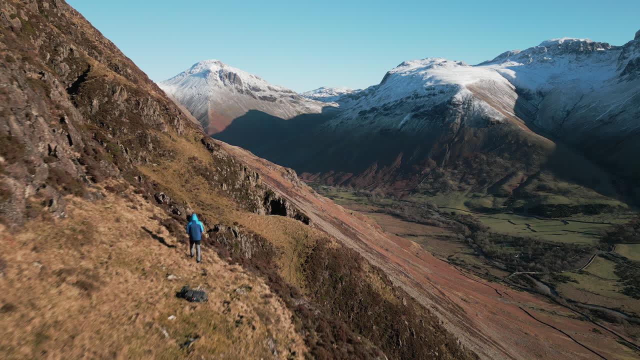 excursionista en la ladera de la montaña con montañas nevadas en la distancia y el valle verde revelan en el distrito del lago wasdale uk