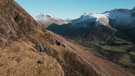 hiker on mountainside with snowy mountains in distance and green valley reveal at wasdale lake district uk