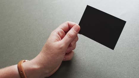 Hand-of-caucasian-woman-holding-black-business-card-on-grey-background,-copy-space,-slow-motion