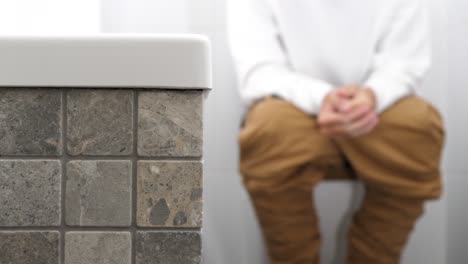 a man with trousers down sitting on the toilet has problems with defecation or kidney stones, he is uptight, clenches his fists.
