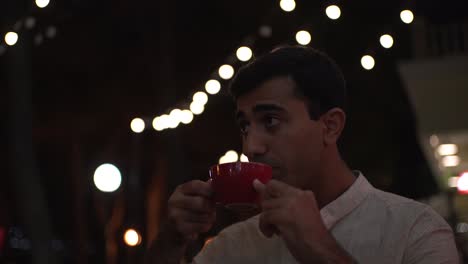 man drinking coffee at an outdoor cafe at night