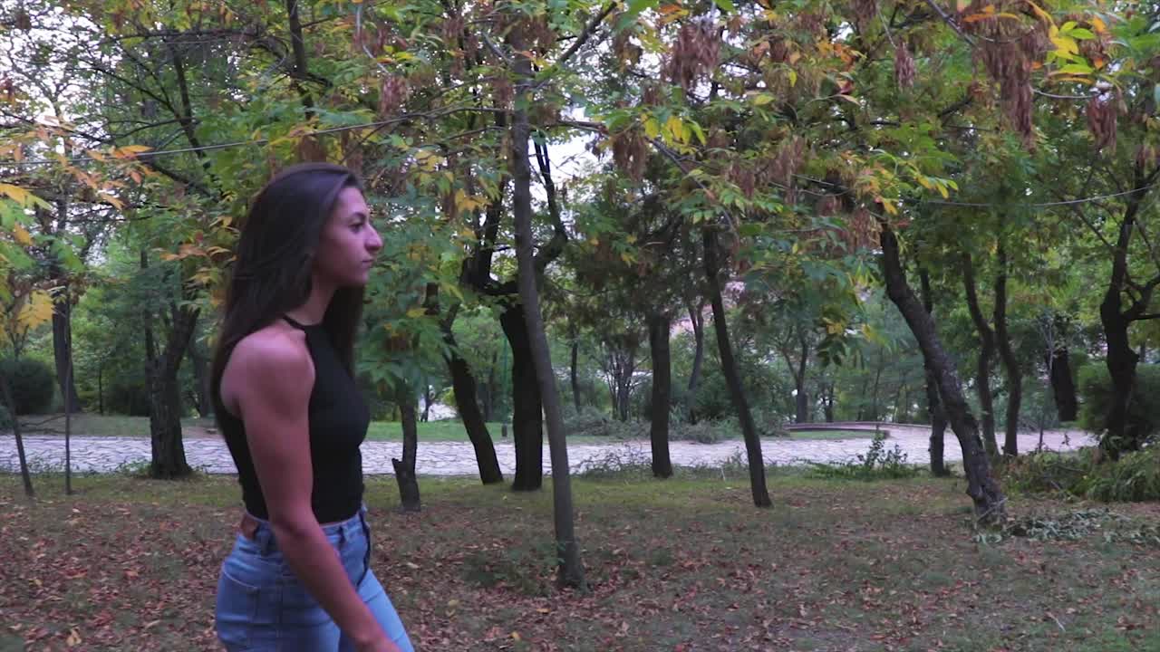 hermosa joven modelo caminando en un parque con árboles con hojas verdes