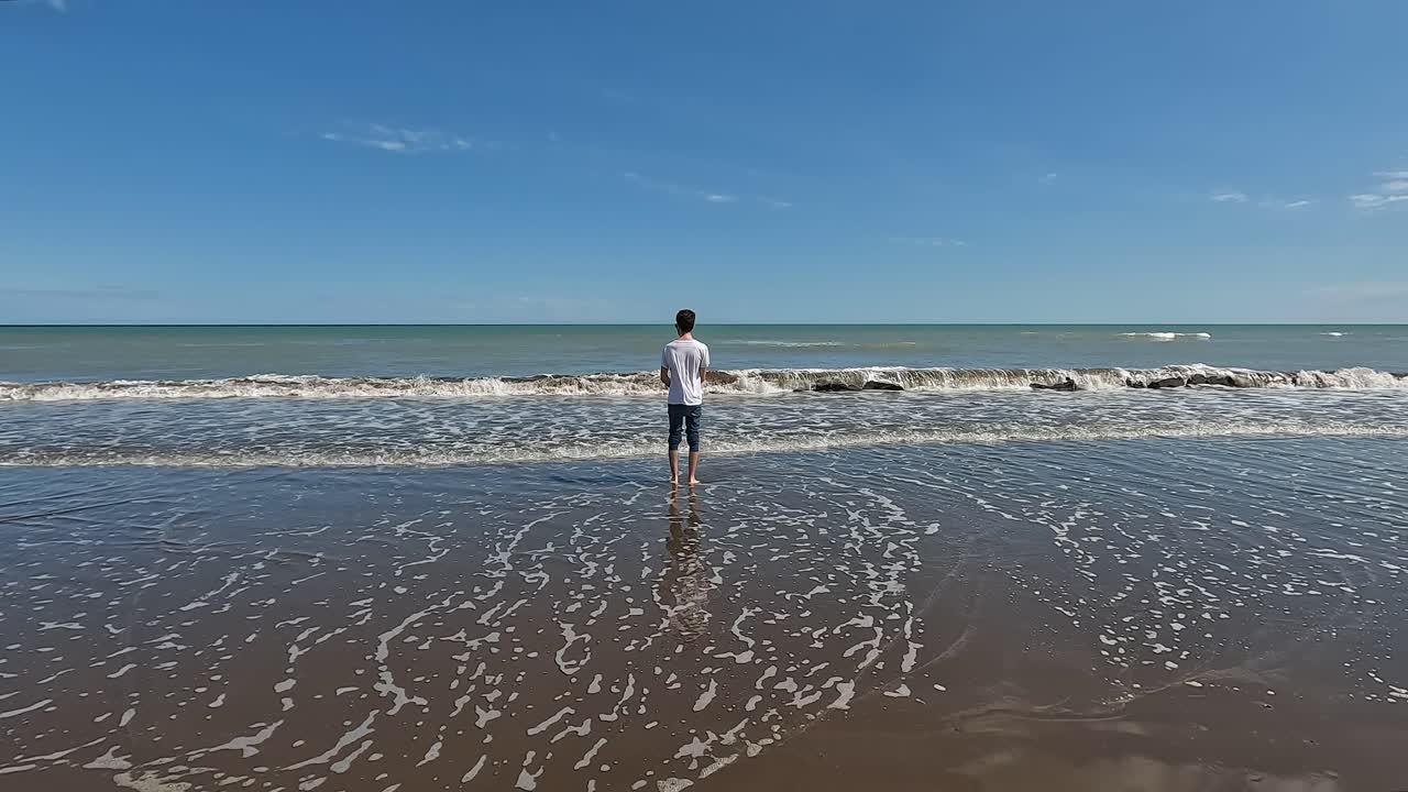 아르헨티나 몬테 에르모소에서 튀는 파도와 함께 해안에 서 있는 남성 관광객