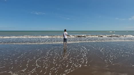 Turista-Masculino-De-Pie-En-La-Orilla-Con-Olas-Salpicando-En-Monte-Hermoso,-Argentina