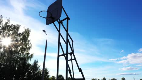 Silhouette-of-old-basketball-hoop-against-blue-sky,-low-angle-view