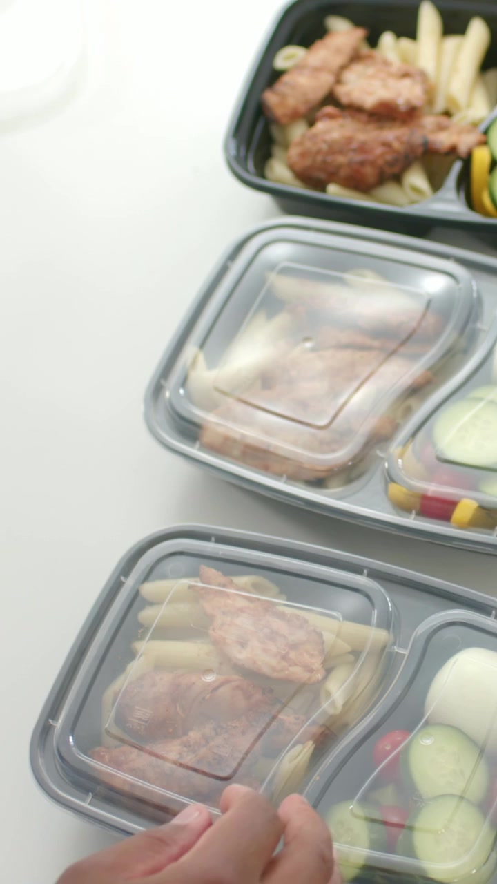 Uomo che allunga la mano e sigilla coperchi trasparenti su tre contenitori per la preparazione dei pasti con penne e pollo